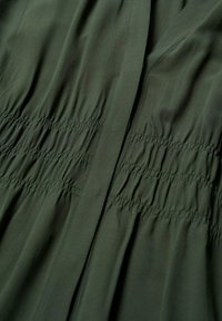 Vihreä, kevyt kangas, jossa on kerrostumaa, pystysaumojen kanssa ja sileä tekstuuri. Ei näkyviä kuvioita tai varusteita.
