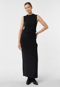 Czarna sukienka bez rękawów, do kolan, wykonana z teksturowanej, błyszczącej tkaniny. Posiada wysoki dekolt i dopasowaną sylwetkę.