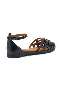 Zapato plano de cuero negro con un diseño trenzado, tira en el tobillo y perfil bajo. Presenta una textura suave y una plantilla marrón.