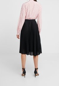 Gonna nera plissettata con una finitura texturizzata, abbinata a una camicia a maniche lunghe rosa chiaro con pois neri. Scarpe con tacco nere.