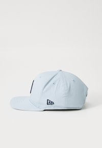 Jasnoniebieska czapka bejsbolowa z płaskim daszkiem, wykonana z tkaniny, z granatowym haftowanym logo z przodu i z boku. Sześciopanelowy design.