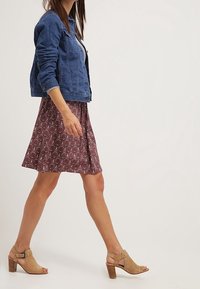 Modrá džínová bunda, burgundské šaty s květinovým vzorem a béžové sandály na podpatku. Oblečení má rozšířenou sukni a otevřenou špičku.