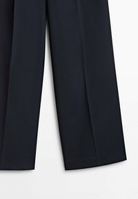 Pantalon bleu marine sur mesure avec jambes droites, plis visibles et tissu subtilement texturé sur un fond blanc uni.