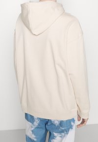 Beige huppari, jossa on rento istuvuus, pehmeä pinta ja resorit hihansuissa. Yhdistetty sinisiin pilvikuosisii housuihin.