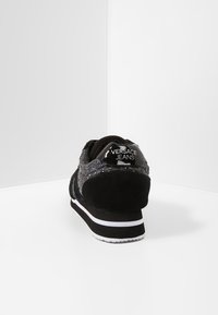 Baskets noires avec une tige texturée ornée de accents pailletés, des détails en daim, et un passant de talon noir brillant embossé du texte "Versace Jeans".