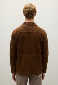 Giacca in suede marrone con collo a rever, cucitura del giogo posteriore e maniche lunghe, caratterizzata da una texture liscia e un design semplice.