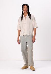 Hellbeige Kurzarm-Hemd mit Knopfverschluss und Karomuster, kombiniert mit hellblauen Jeans und beigen Sneakers. Einfaches, lässiges Design.