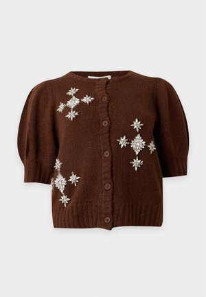 Jeune femme portant un cardigan marron à manches courtes avec broderie florale, un pantalon large gris et des chaussures compensées marron.