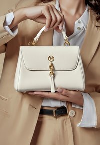Borsa a mano crema con un design strutturato, hardware dorato e una chiusura frontale. La borsa presenta un manico corto e una texture liscia.