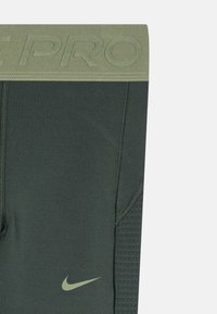 Pánské sportovní legíny v tmavě zelené barvě s texturovanou síťovinou, vybavené světle zeleným elastickým pasem a bílým logem Nike.