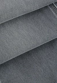 Material denim în nuanțe variate de gri, având o textură de țesătură twill cu detalii de cusătură subtile pe margini.