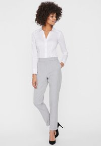 Hvit langermet skjorte med knapper kombinert med lys grå, skreddersydde pinstripe bukser og svarte høye hæler. Enkelt, tilpasset design.
