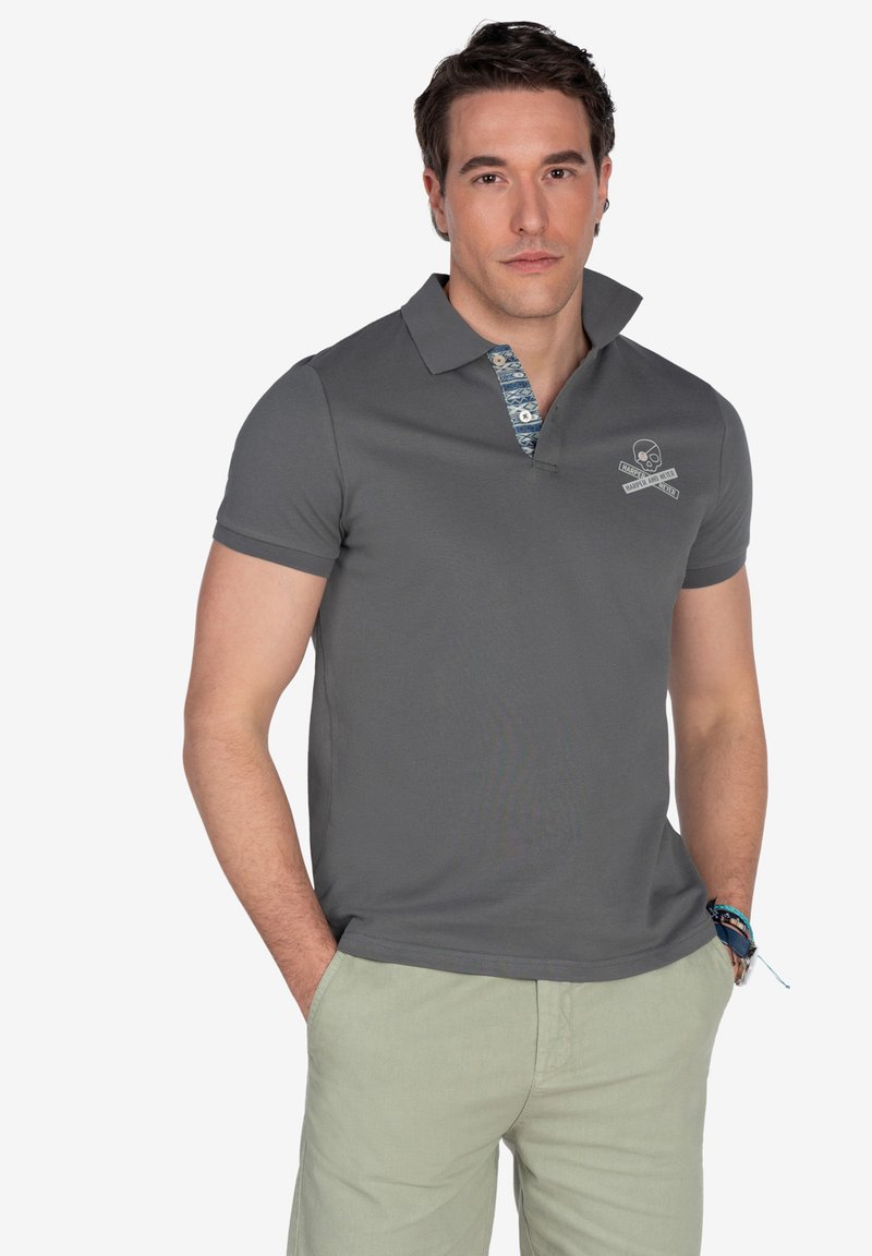 Polo gris con un collar texturizado que presenta un patrón azul y blanco. Pequeño logo de calavera en el pecho. Mangas cortas, tejido suave.