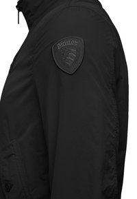 Black textured jacket featuring a woven patch with the "Blauer" logo on the left shoulder, side pockets, and a high collar design.
