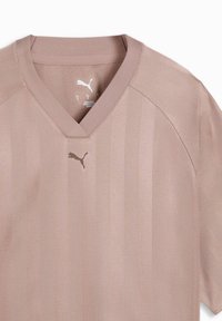 Αθλητική μπλούζα σε μωβ χρώμα με V-λαιμόκοψη και κοντά μανίκια, με διακριτικές κάθετες ρίγες και μικρό λογότυπο Puma στο κέντρο κάτω από το λαιμόκοψη.