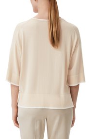 Beżowy sweter dzianinowy o luźnym kroju, z opadającymi ramionami i krótkimi rękawami. Posiada kontrastowe białe wykończenie wzdłuż brzegów.