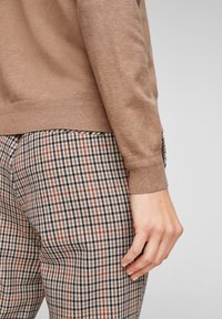 Brązowy sweter dziany z prążkowanymi mankietami, połączony z kraciastymi spodniami w odcieniach beżu, brązu i czerni, o teksturowanym, kratkowanym wzorze.