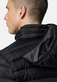 Zwarte pufferjack met hoge kraag, textuurstof en ritsaccenten. Het interieur heeft een gladde afwerking en contrasterende matte details.
