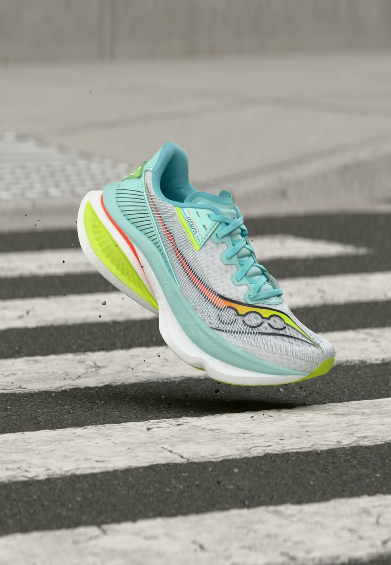 Ανοιχτό μπλε και λευκό αθλητικό παπούτσι με νέον κίτρινες και πορτοκαλί λεπτομέρειες να αιωρείται πάνω από διάβαση πεζών σε άσφαλτο.