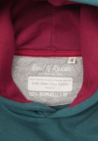 Hættebluse med en teal farve og maroon foer. Etiketten angiver 100% økologisk bomuld, produceret under Global Organic Textile Standard.