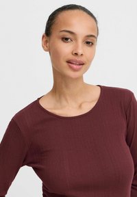 Burgundin värinen muotoiltu paita, jossa on pyöreä kaula-aukko, ribbaustekstuuria ja pitkät hihan, esittelee hienovaraisia pystysuoria viivoja kankaan pinnalla.
