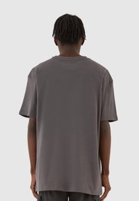 Overdimensioneret grå bomulds-T-shirt med rund halsudskæring og korte ærmer. Glat tekstur uden synlige mønstre eller hardware detaljer.