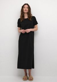 Black, short-sleeve maxi dress with a relaxed fit and side slit; made of soft fabric, paired with knotted, natural-colored sandals.