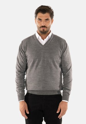 Maglione grigio lavorato a maglia con scollatura a V, maniche lunghe e polsini a costine. Indossato sopra una camicia bianca con colletto, abbinato a pantaloni neri.
