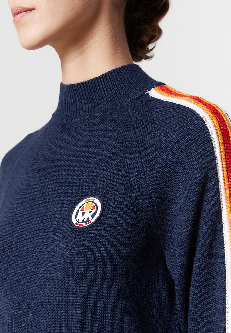 Navy gebreide trui met een hoge hals, voorzien van kleurijke strepen in rood, oranje en wit langs de mouwen en een logopatch op de borst.