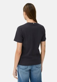 Donkergrijze katoenen t-shirt met korte mouwen, een ronde hals en een klein accent op de achterkant. Gecombineerd met lichtblauwe wijde denim jeans.