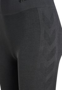 Nahaufnahme von schwarzen nahtlosen Leggings mit strukturierten Chevron-Mustern entlang des äußeren Oberschenkels und einem breiten Bund.