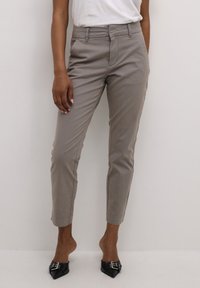 Graue, schmal geschnittene Hose mit flachem Bund, Gürtelschlaufen, vorderen Taschen und glatter Textur, kombiniert mit schwarzen spitzen Ballerinas.