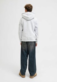 Sudadera gris claro con una costura central en la parte posterior y una gran capucha, combinada con jeans oscuros de pierna ancha y calzado beige.