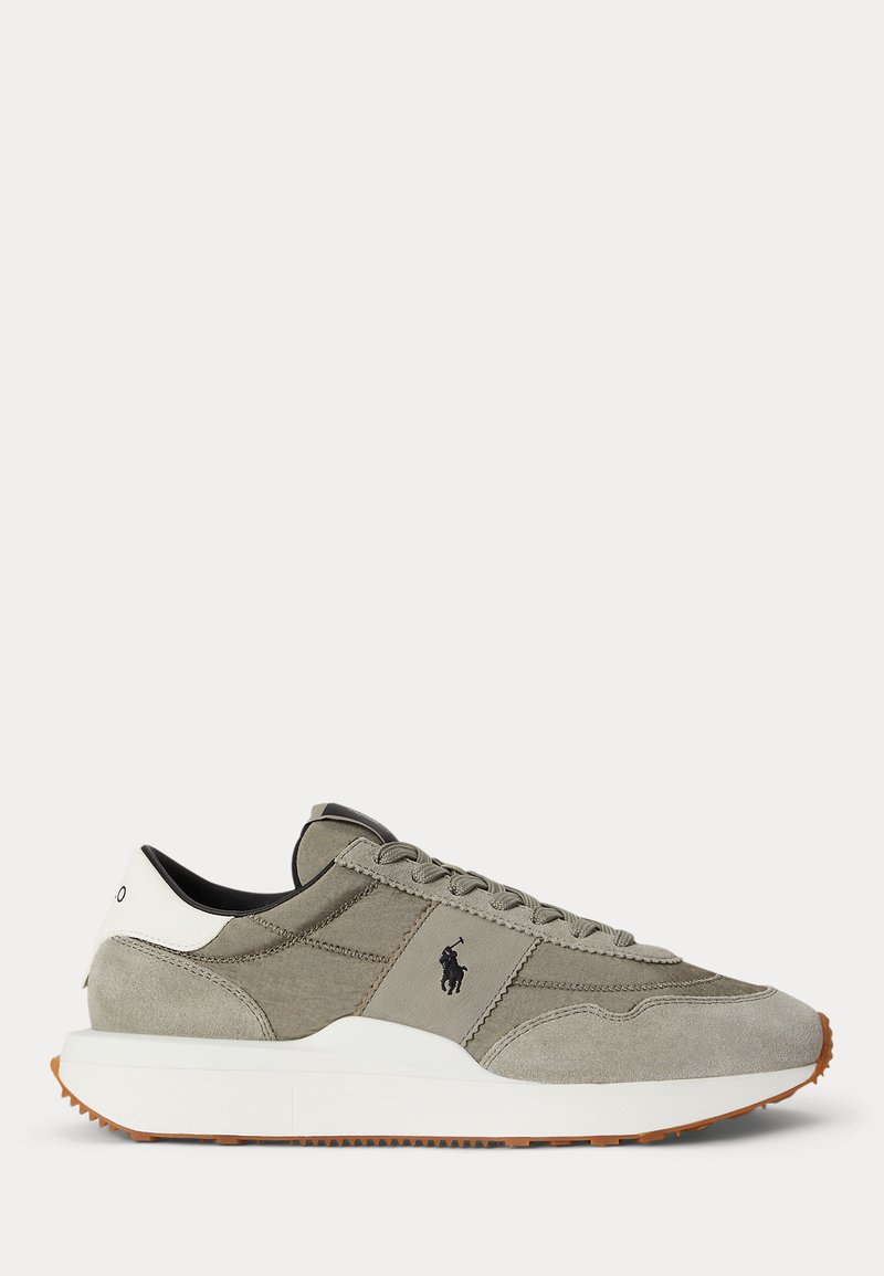 Ανοιχτό γκρι sneaker από σουέτ και ύφασμα με λευκή σόλα και μαύρο λογότυπο στο πλάι, καφέ λαστιχένια εξωτερική σόλα και λευκή γλωττίδα με μαύρο κείμενο.