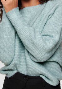 Helles Blau, oversized Pullover aus weichem Strickstoff mit gerippten Bündchen, der eine lässige Passform und ein strukturiertes Muster zeigt.