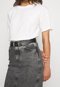 Valkoinen puuvillapaidan lyhyet hihat ja hillitty logo-ommel, yhdistettynä korkeavyötäröiseen mustaan farkkuhameeseen, jossa on suora siluetti.