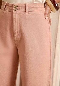 Roze denim broek met een hoge taille, dubbele knoopsluiting en een subtiele textuur. Zijkanten met zakken zijn zichtbaar, wat het ontwerp verbetert.