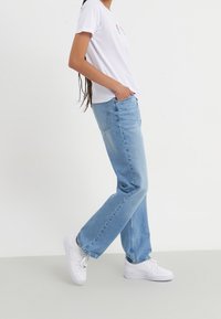 Vaqueros de corte recto en azul claro, fabricados en algodón, de cintura media, y una camiseta de cuello redondo blanca con bordado floral. Zapatillas blancas.