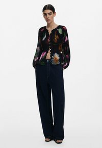 Svart blommig blus med lång ärm, med livfulla blommönster, knappframsida och genomskinligt tyg. Kombinerad med hög midja mörka jeans.