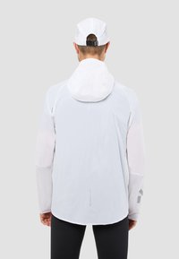 Biała lekka kurtka z dopasowanym kapturem, siateczkowymi akcentami i kontrastowymi rękawami. Gładka tekstura z odblaskowym logo na plecach.