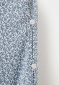 Blaues und weißes Stoffmuster mit zwei weißen Knöpfen, die vertikal nahe am Rand auf einem hellen Hintergrund angenäht sind.