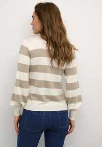 Knitted sweater in cream with beige horizontal stripes, featuring puffed sleeves and a fitted hem. Worn with blue jeans.