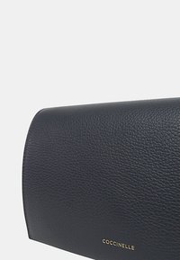Borsa a frizione in pelle blu scuro con superficie texturizzata, forma arrotondata e logo del marchio in oro. Presenta una chiusura a patta sicura.