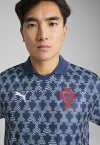 Maillot de soccer bleu foncé avec un motif texturé de formes bleu clair, orné d'un écusson national rouge et d'un logo Puma blanc sur le côté gauche.
