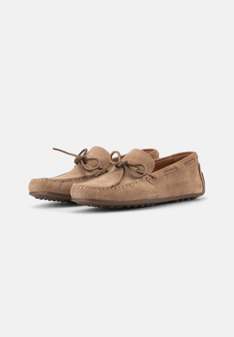 Lichtbruine suède mocassin loafers met afgeronde neuzen, gestikte details en gebonden leren veters tegen een witte achtergrond.