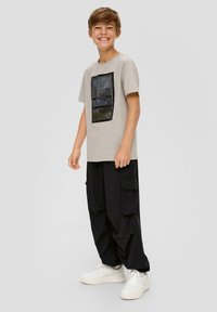 Hellgraues T-Shirt mit einem strukturierten schwarzen quadratischen Design, das eine Landschaft darstellt, kombiniert mit lockeren schwarzen Cargo-Hosen und weißen Sneakers.