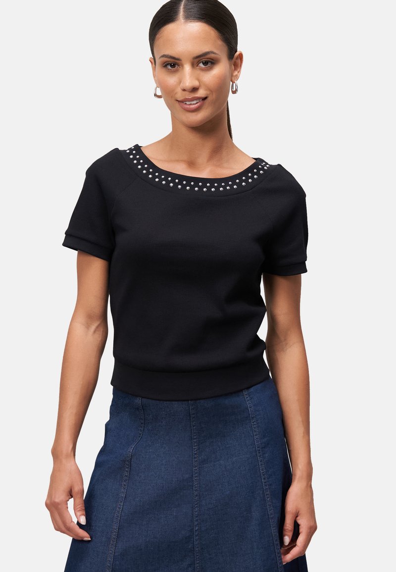 Zwarte top met korte mouwen en een ronde halslijn, versierd met zilveren studs, gemaakt van een gladde stof, gecombineerd met een denim blauwe rok.