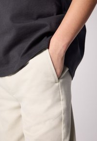 Szürke pamut póló, amely részben takarja a krémszínű pamut nadrágot, oldalzsebbel. A pólón kerek nyakkivágás és rövid ujjak vannak.