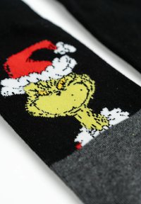Calzini neri con un design del Grinch giallo e un cappello di Babbo Natale rosso. Bordo caviglia grigio e accenti di fiocchi di neve bianchi. Materiale a maglia morbido.
