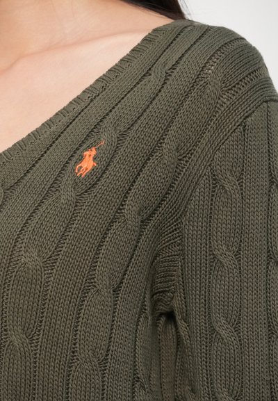 Olivovo zelený pletený sveter s vrkočovým vzorom a výstrihom do V. Má vyšívané oranžové logo na ľavom hrudi.
